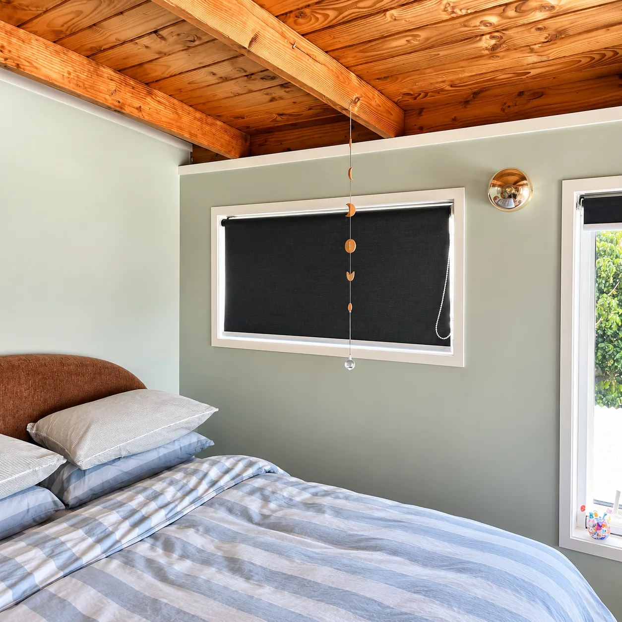 Sage green bedroom with black roller blinds under a timber ceiling